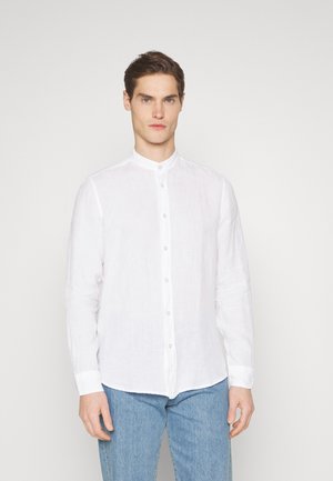 Camisa de lino blanca con cuello tipo banda, cierre frontal de botones y mangas largas. Combinada con jeans de mezclilla azul claro. Diseño simple y texturizado.
