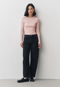 Light pink long-sleeve ribbed top paired with high-waisted black wide-leg jeans. Features flat front pockets and classic footwear.