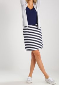 Lyhythihainen harmaa neuletakki, laivastonsininen paita ja valko-/laivastonsininen raidallinen hame. Yhdistetty valkoisiin lenkkareihin. Yksinkertainen, rento muotoilu, kevyt kangas.