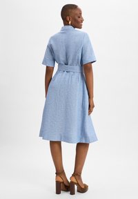 Light blue short-sleeve dress with a belted waist, featuring a textured fabric and a flared skirt, paired with brown platform heels.