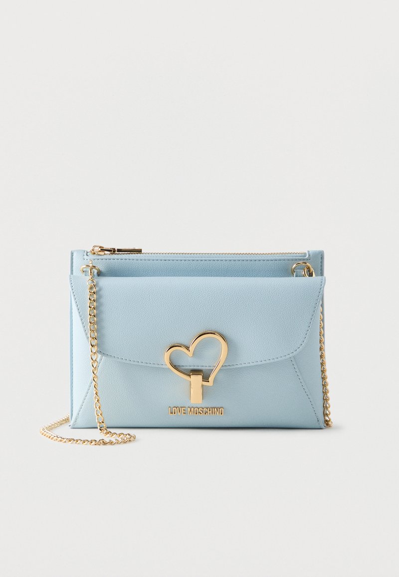 Ανοιχτό μπλε τσάντα Love Moschino με χρυσό κούμπωμα σε σχήμα καρδιάς και λουράκι αλυσίδα σε λευκό φόντο.