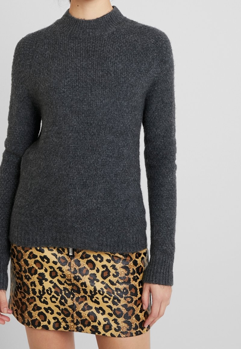 Dunkelgrauer gestrickter Pullover mit hohem Kragen, langen Ärmeln und gerippter Textur, kombiniert mit einem goldenen Leopardenmuster-Rock.
