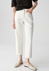 Pantaloni bianchi in cotone con una vestibilità classica, dotati di chiusura anteriore con bottone, tasche laterali e lunghezza cropped. Abbinati a mocassini beige.