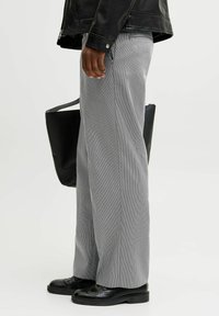 Hallidega hallid laiad püksid tekstuuriga kangast, koos mustade kingade ja musta käekotiga.