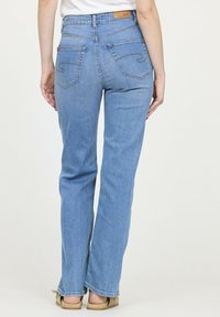 Jean en denim bleu avec une coupe droite, couture visible, deux poches et une étiquette beige à la taille.