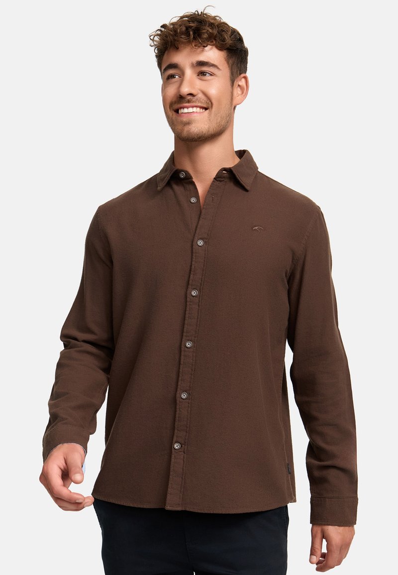 Camisa marrón de manga larga hecha de una tela suave, presenta un cuello clásico, cierre frontal con botones y un pequeño logo en el pecho.