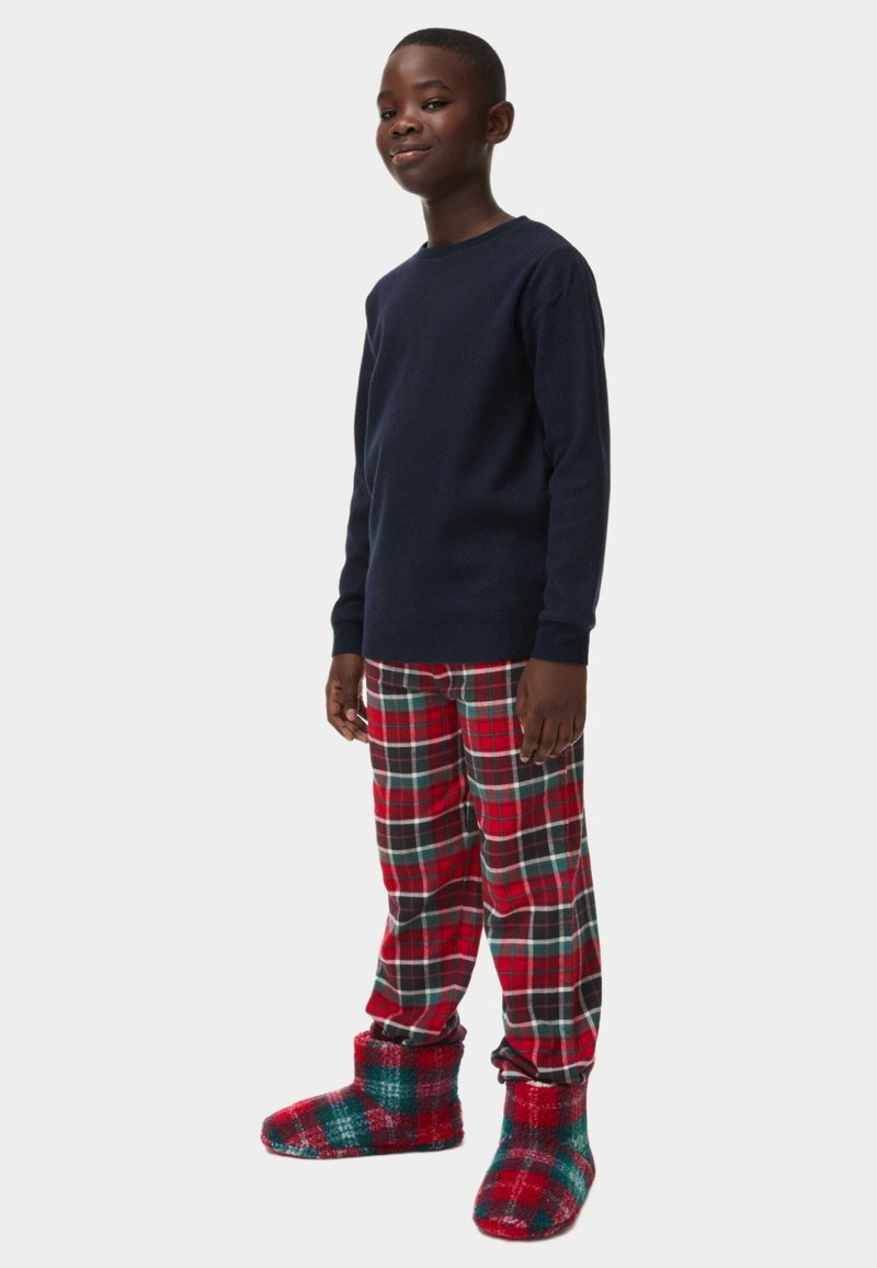 Marineblaues Langarmshirt, rot und grün karierte Schlafanzughosen und flauschige rote Hausschuhe mit grünen Akzenten. Weiche, warme Materialien für Komfort.