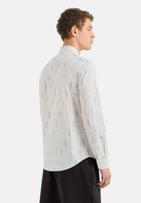 Camicia a maniche lunghe con bottoni in tessuto bianco, caratterizzata da righe verticali e accenti neri sparsi, con orlo curvo e colletto classico.