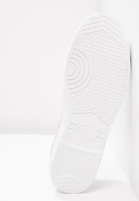 Suola di sneaker bianca caratterizzata da un motivo testurizzato, elementi di design circolari e dettagli di branding. Il materiale sembra essere gomma con una finitura liscia.