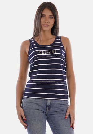 Donna che indossa un top senza maniche a righe blu navy e bianche con la scritta "YES ZEE", abbinato a jeans azzurri, in piedi su sfondo bianco.