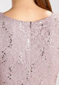 Krajková šaty v světle růžové barvě s propracovanými květinovými vzory a flitry. Obsahuje skrytý zip na zadní straně. Celkově měkká textura.