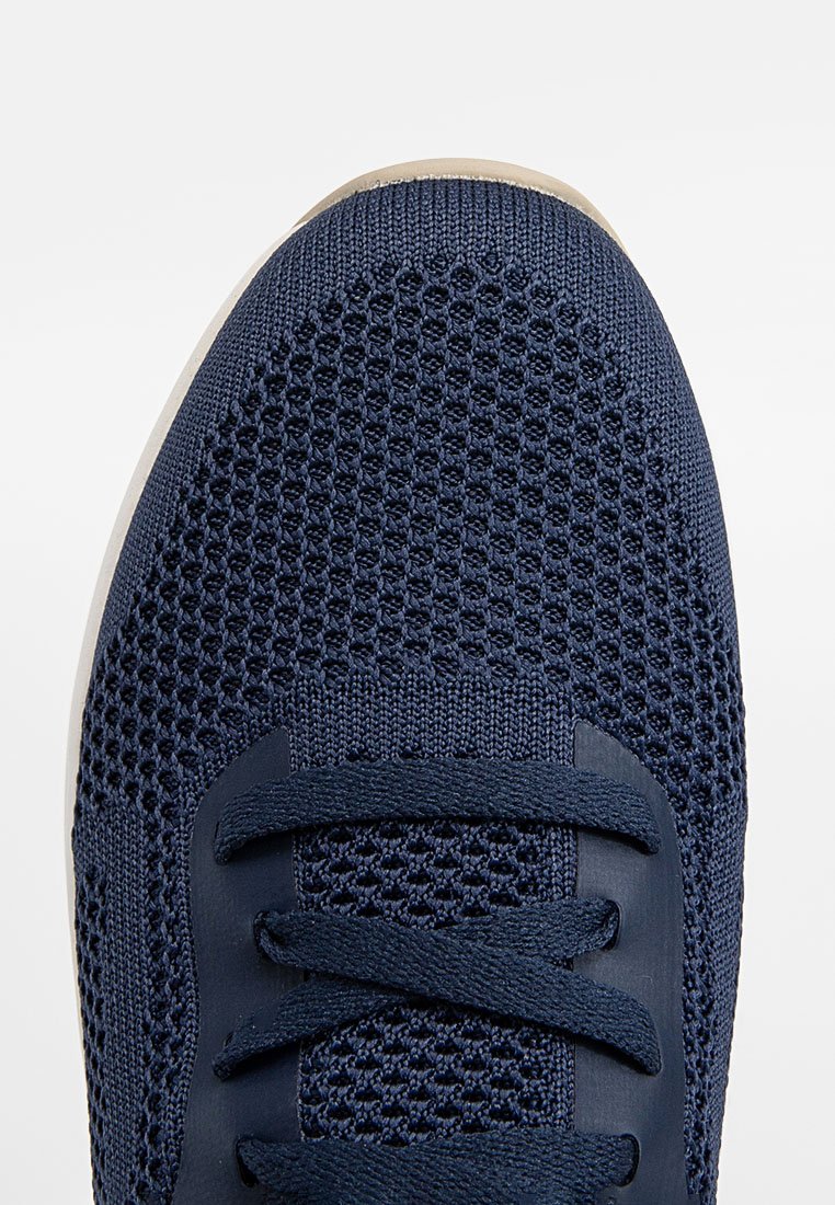 Granatowe buty sportowe z przewiewną siateczką na górze, okrągłym noskiem i płaskimi sznurówkami. Posiadają teksturowany wzór na górze oraz lekką podeszwę.