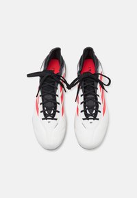 White soccer cleats with black laces and accents, featuring red diagonal stripes on the sides and a textured upper for grip.