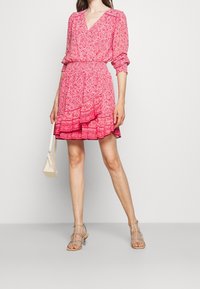 Blommönstrad rosa klänning med v-ringning, långa ärmar och volangkant. Kombinationen med sandaletter med genomskinliga remmar och en liten handväska i krämfärg.