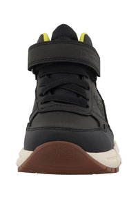 Zapatilla deportiva negra con parte superior texturizada, correa de velcro y cordones redondos. Cuenta con una suela de goma y una entresuela beige clara en contraste.