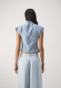 Light blue cropped top with cap sleeves, smooth texture, and a high back collar. Paired with light gray wide-leg trousers.