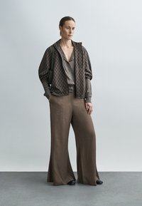 Veste marron à motifs avec fermeture éclair sur un haut marron assorti et un pantalon large. Tissu texturé avec de grandes manches et un design minimaliste.