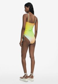 Costum de baie întreg, cu un gradient de la galben la verde; bretele subțiri ajustabile, detalii drapate și accente cu legături pe lateral. Material neted și elastic.