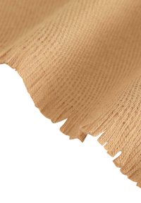 Luonnonvärinen, teksturoitu kangas, jossa on kudottu kuvio ja epätasaiset frangeet. Pehmeä, hieman karkea pinta, jossa näkyvät kuidut.