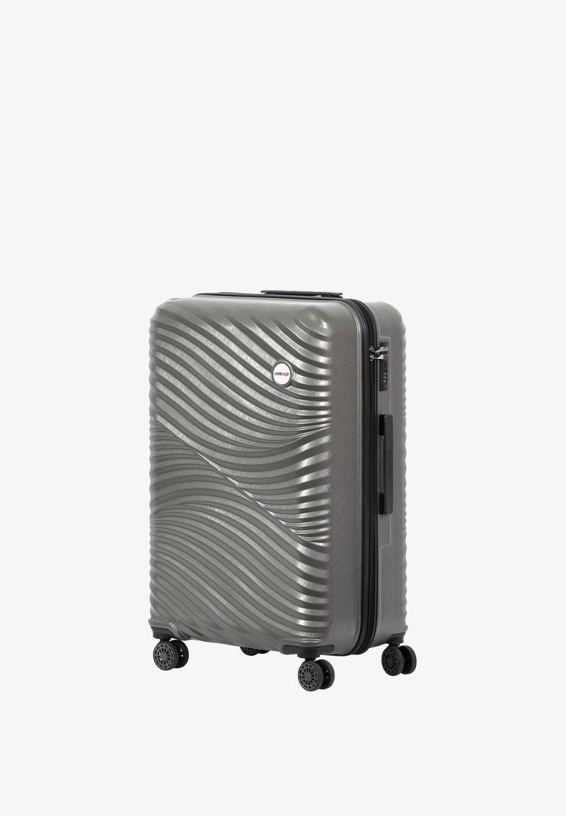 Hard-shell gray suitcase with wavy texture, four black wheels, top handle, and zipper closure. Features a small circular logo on the front.