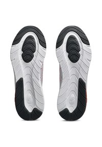 Semelles de chaussures de sport noir et blanc avec un motif de traction texturé, dotées d'une rainure centrale et d'accents rouges sur les côtés.