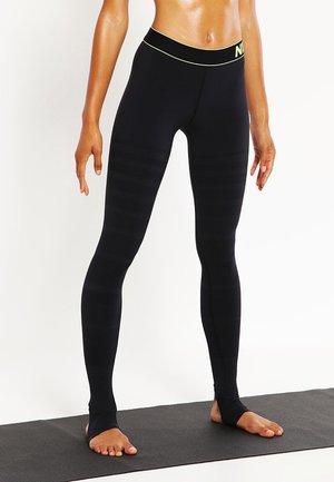 Leggings noirs en matière lisse et extensible avec une taille haute, présentant une texture côtelée discrète et un logo jaune fluo sur la taille.