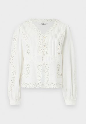 Blouse blanche à manches longues avec découpes en dentelle florale, bords festonnés, plis verticaux cousus et fermeture boutonnée à l'avant.