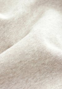 Tejido beige claro con una suave textura entrelazada, que presenta un patrón sutil y ligeramente irregular, además de un acabado liso.