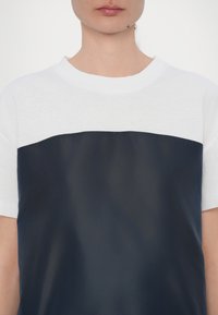 T-shirt en mélange de coton avec une section supérieure blanche et une section inférieure en bleu marine brillant. Dispose d'un col rond et de manches courtes.