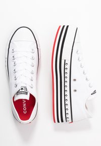 Vita canvassneakers med en tjock plattform, med svarta och röda randiga detaljer, silverfärgade öglor och en röd innersula.