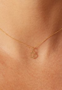 Gold necklace with a thin chain and a small, shiny, uppercase "D" pendant. The surface is smooth, with no visible embellishments.