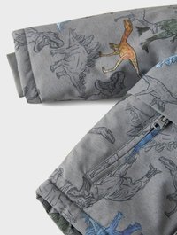 Grått tyg med ett dinosauriemönster i olika färger. Designen inkluderar detaljerade illustrationer av olika dinosauriearter.