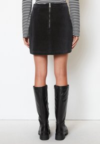 Gonna di velluto a coste nera con zip sul retro, abbinata a stivali in pelle nera al ginocchio con zip laterali e suola spessa.