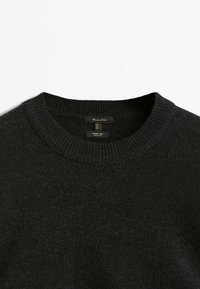 Pull gris foncé à côtes avec col rond en fil de laine d'agneau, avec étiquettes de marque et de matériau visibles à l'encolure.