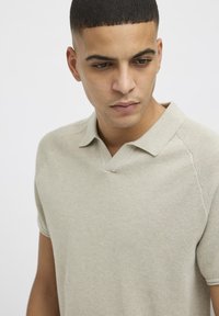 Beige strikket polo skjorte med teksturert overflate, v-hals og korte ermer. Har raglan-sømdesign for ekstra stil og komfort.