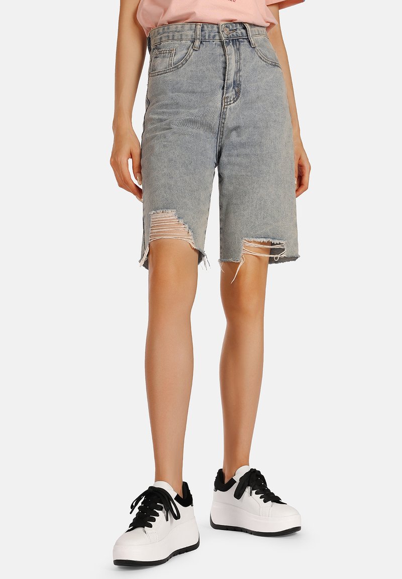 I pantaloni bermuda in denim azzurro chiaro presentano orli sfrangiati e dettagli strappati. Abbinati a sneakers bianche con lacci neri.