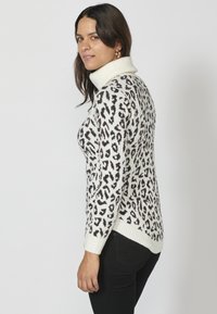 Vit polotröja med svart leopardtryck, ribbade ärmslut och nederkant. Bärs tillsammans med svarta jeans med avslappnad passform och texturerad stickning.