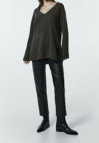 Brun v-hals sweater med lange ærmer, struktureret strik, kombineret med sorte læderbukser med smalle ben og ankelstøvler, mod en hvid baggrund.