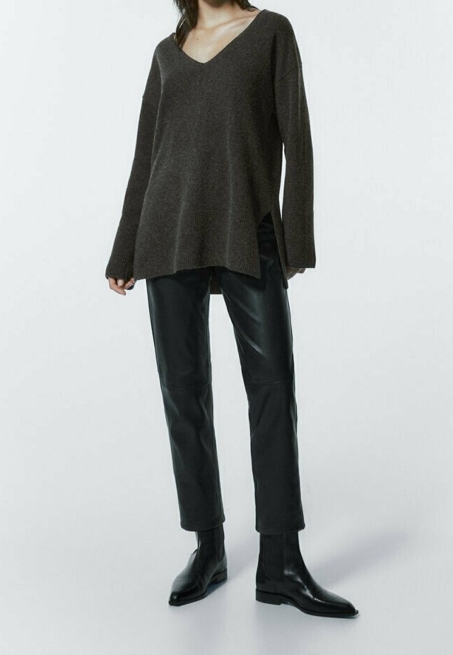 Brun v-hals sweater med lange ærmer, struktureret strik, kombineret med sorte læderbukser med smalle ben og ankelstøvler, mod en hvid baggrund.