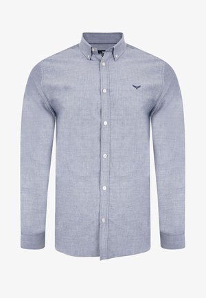 Lyseblå skjorte med knaplukning lavet af bomuld. Har en krave, standard knapper og et broderet logo på venstre bryst. Lange ærmer.