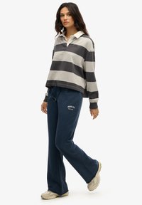 Paski długi rękaw polo w odcieniach szaro-niebieskich z kołnierzykiem, w połączeniu z granatowymi spodniami dresowymi z napisem "BROOKLYN". Całość dopełniają tanowe sneakersy.