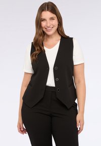Gilet nero con un design sartoriale, caratterizzato da scollo a V, chiusura a tre bottoni e tasche laterali, indossato su una t-shirt bianca.