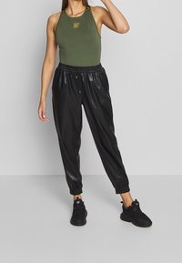 Top senza maniche verde oliva con logo ricamato e pantaloni jogger neri con vita elasticizzata, di forma affusolata, texture lucida e polsini alle caviglie.