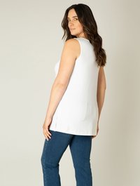 Witte mouwloze top met een relaxte pasvorm en zijsplitten, gecombineerd met blauwe denim jeans. Gladde stof, minimalistisch ontwerp.