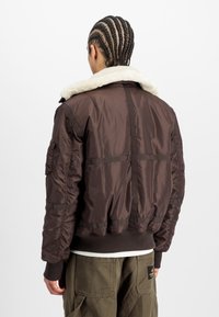 Chaqueta bomber marrón con un cuello de borreguito, puños y dobladillo acanalados, y bolsillos laterales. Tejido suave y acolchado con un diseño recortado.