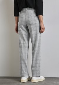 Grå rutiga byxor med hög midja, avslappnad passform och slät yta. Matchas med vita sneakers. Bakifrån syns två bakfickor.