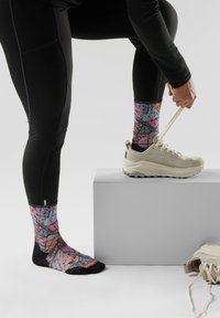 Calzini colorati a fantasia con un mix di rosa, blu e nero, abbinati a una sneaker beige. I calzini presentano un design nero sulla punta e sulla caviglia.
