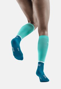 Calze a compressione in gradiente teal e blu, con un motivo testurizzato e un design aderente, complete di un accento bianco nella parte superiore.