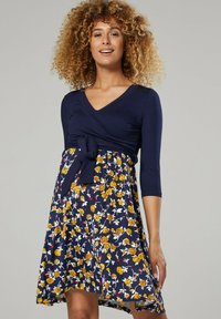 Navy blue dress with a wrap design and three-quarter sleeves, featuring a floral pattern in yellow and white on the skirt. Includes a tied waist detail.