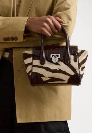 Personne portant un manteau beige tenant un petit sac à main imprimé zèbre avec des garnitures en cuir brun foncé et un fermoir argenté.